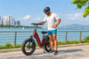 Helmeted rider looking at the handlebars of a red electric bike beside a waterfront
